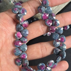 Puede incluir: Un hilo de cuentas facetadas en forma de corazón con una mezcla de tonos azul profundo y rosa magenta vibrante. Las cuentas están ensartadas con una borla decorativa en la parte superior, mostrando un acabado pulido que refleja la luz.
