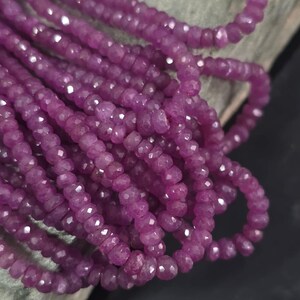 May include: Strands of faceted, deep magenta beads. The beads are strung together, creating a flowing, textured appearance. The beads have a polished, reflective surface, catching the light and creating a sparkling effect. The beads are likely gemstones, suitable for jewelry making.