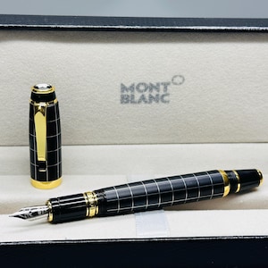 May include: A black fountain pen with a white grid pattern and gold-tone accents, featuring a metal nib and a matching cap with a gold clip. The pen is displayed inside a black presentation box with the Montblanc logo printed on the interior lining.