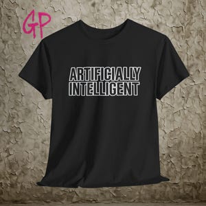 May include: Black t-shirt featuring the text "ARTIFICIALLY INTELLIGENT" in white, outlined letters. The shirt has short sleeves and a crew neck. The letters "GP" are in pink in the upper left corner.