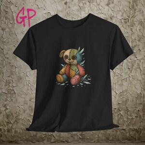 Könnte beinhalten: Schwarzes T-Shirt mit einem bunten Patchwork-Teddybär-Design. Der Bär hat Knopfaugen und ist von stilisierten kristallartigen Elementen umgeben. Das Design ist mittig auf dem Shirt platziert und bietet einen einzigartigen, künstlerischen Look.