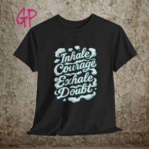 Könnte beinhalten: Schwarzes T-Shirt mit dem Schriftzug "Inhale Courage Exhale Doubt" in Weiß und Türkis, umgeben von Wolkenmotiven. Das T-Shirt hat kurze Ärmel und einen Rundhalsausschnitt.