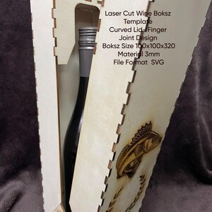 Puede incluir: Una caja de vino de madera cortada con láser con un diseño de pez y el texto "Laser Cut Wine Boksz Template". La caja está diseñada con una tapa curva y un diseño de junta a inglete. Tamaño de la caja 10x10x32 cm.