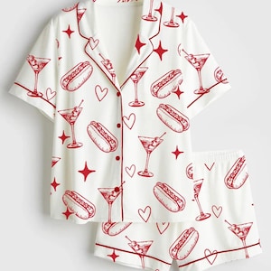May include: White pajama set with a red print of hot dogs, martini glasses, hearts, and stars. The short-sleeved top and shorts have red trim. The button-down shirt has a notched collar.