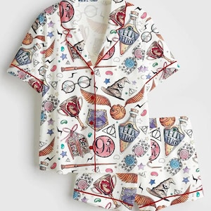 May include: White pajama set with a repeating pattern of Harry Potter-themed graphics, including potion bottles, glasses, and the number 9 3/4. The set features a short-sleeved top and shorts, both trimmed with red piping.