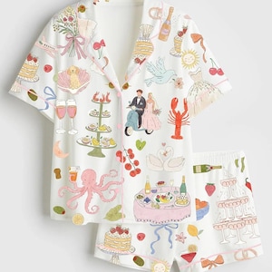 May include: White pajama set with a whimsical wedding theme print. The short-sleeved top and shorts feature illustrations of cakes, champagne, a bride and groom, and other celebratory elements. The set is trimmed with pink piping.