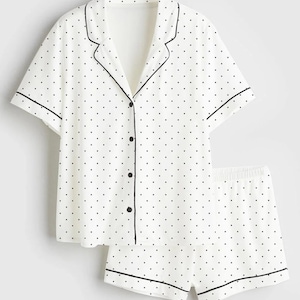 May include: White pajama set with black polka dots. The short-sleeved top has a notched collar and black trim. The matching shorts have an elastic waistband and black trim. The set is made of a lightweight fabric.