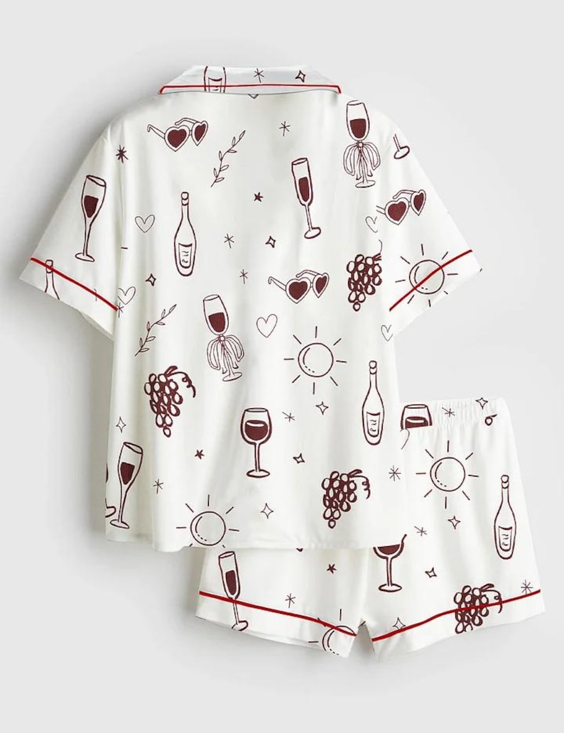 May include: White pajama set with a wine-themed pattern. The short-sleeved top and shorts feature a repeating design of wine glasses, bottles, grapes, and sunglasses. Red trim accents the edges of the set.