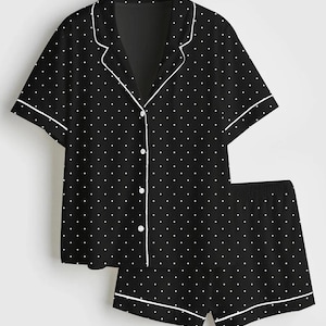 May include: Black pajama set with white polka dots. The short-sleeved top has a notched collar and button-down front. The shorts have an elastic waistband. Both pieces are trimmed with white piping.