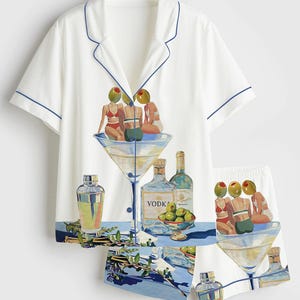May include: White pajama set with a blue trim. The set features a whimsical illustration of a martini glass with three figures, olives, and bottles of liquor. The shorts and shirt have the same design.