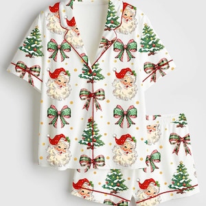 May include: White Christmas-themed pajama set featuring a short-sleeved top and shorts. The set is adorned with Santa Claus faces, Christmas trees, and plaid bows. The edges are trimmed with red piping.