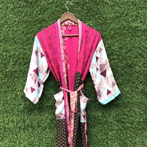 Puede incluir: Una bata de manga larga con un diseño de patchwork que combina paneles de tela en rosa vibrante, marrón oscuro y blanco. La prenda incluye un cinturón a juego en la cintura, dos bolsillos delanteros y un estampado de triángulos y cachemir.