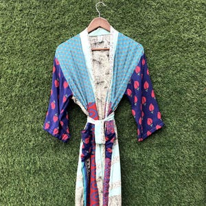 May include: A long-sleeved robe featuring a patchwork design with various patterns and colors, including blue, red, and cream. The garment has a tie-waist belt, two front pockets, and a wide collar, constructed from multiple fabric panels.