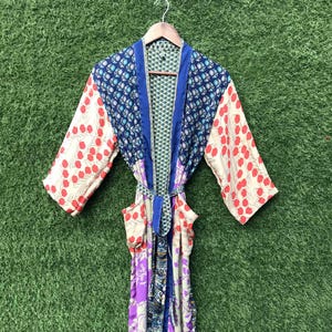 May include: A long-sleeved robe featuring a patchwork design with various floral and geometric patterns in shades of blue, red, purple, and cream. The garment includes a matching fabric tie belt at the waist and two front pockets on the lower section.