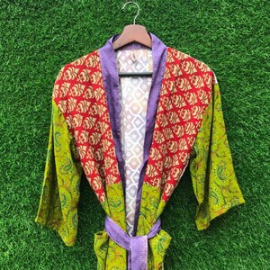 May include: A colorful robe with a floral pattern in red and gold, green paisley sleeves, and a purple collar and belt. The robe is hanging on a wooden hanger against a green background.