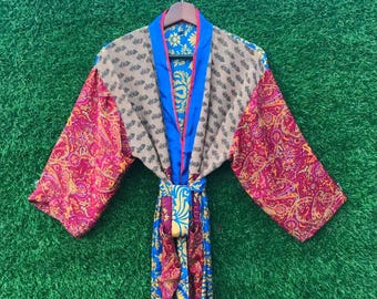 May include: A colorful, patterned robe with a paisley design in shades of pink, red, and yellow. The robe has a blue trim and a matching belt. The sleeves are long and wide, and the robe is hanging on a wooden hanger.