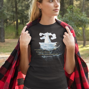 Puede incluir: Camiseta negra con un gr&aacute;fico de velero y la cita "So we beat on, boats against the current, borne back ceaselessly into the past" de El Gran Gatsby. La camiseta se usa con una franela a cuadros roja y negra.