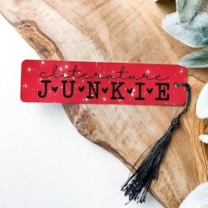 Red metal bookmark with sparkles.  In black is the quote “Clitature Junkie”.