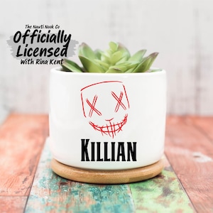May include: A white ceramic mug with a black handle and the text "But First, Coffee" in a bold, black font. The mug is set against a blurred background, suggesting a cozy setting.