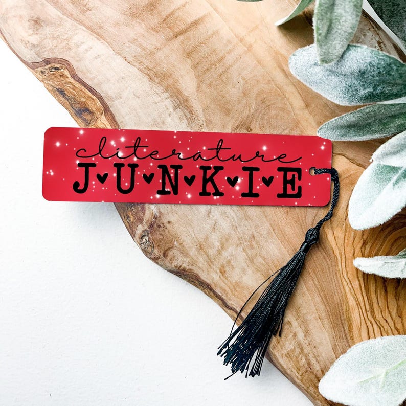 Red metal bookmark with sparkles.  In black is the quote “Clitature Junkie”.