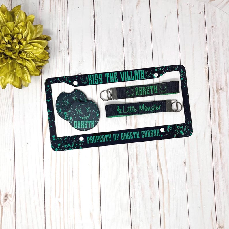May include: A black license plate frame with green splatter design, the text "KISS THE VILLAIN" and "PROPERTY OF GARETH CARSON". Includes matching car coasters and keychains with "GARETH" and "Little Monster" text.