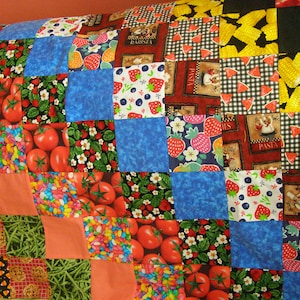 May include: A colorful patchwork quilt with various patterns, including strawberries, tomatoes, candy, and a checkered pattern. The quilt is made of different fabrics and colors, creating a vibrant and playful design.