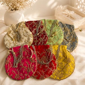 May include: A collection of seven round drawstring pouches in various colors including cream, maroon, light green, grey, fuchsia, red, and yellow. Each pouch features intricate gold floral embroidery and a beaded drawstring closure.