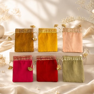 Puede incluir: Seis bolsas rectangulares de tela en colores mostaza, amarillo, melocotón, magenta, rojo y verde oliva. Cada bolsa presenta un borde dorado metálico en la parte superior, un cierre de cordón con pequeñas borlas doradas y acabado liso.