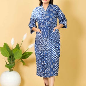 May include: A blue and white patterned robe with a V-neck, three-quarter sleeves, and a matching belt. The robe features a variety of geometric and floral designs. It has two pockets and is knee-length. The model is wearing brown sandals.