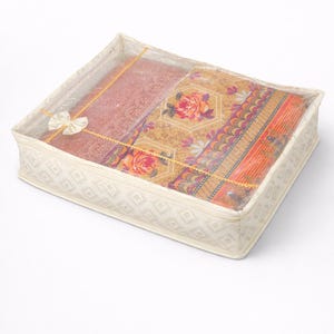 May include: A cream storage box with a clear plastic lid, holding folded textiles. The textiles feature floral and geometric patterns in orange, pink, and yellow. The box is secured with a bow.
