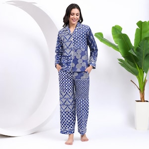 Könnte beinhalten: Ein blau-weiß gemustertes Pyjama-Set. Das langärmlige Oberteil und die Hose weisen verschiedene geometrische Muster auf, darunter Punkte, Kreise und florale Motive. Der Pyjama hat einen Kragen und weiße Zierleisten.