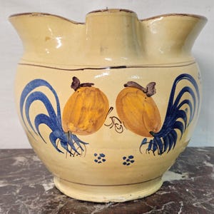 Peut inclure: Un pichet en céramique de couleur crème avec un bord large et festonné ainsi qu'un corps arrondi. L'extérieur présente des illustrations peintes à la main de deux fruits jaunes avec des accents de feuilles bleues et de petits détails floraux bleus.