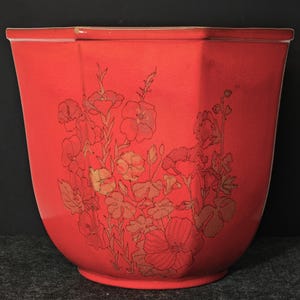 May include: A vibrant red ceramic planter with a floral design. The planter has a geometric shape with a wide opening and a curved base. The floral design is in shades of gold and brown, adding a touch of elegance to the planter.