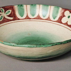 Può includere: Una ciotola in ceramica poco profonda con base color crema, caratterizzata da un bordo interno dipinto a mano decorato con motivi floreali marroni e motivi ad arco verdi. Il centro della ciotola ha una sfumatura verde e il bordo esterno è verde.