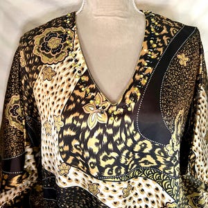 May include: A V-neck tunic with a bold animal print in shades of brown, black, and tan. The tunic features a floral pattern and is embellished with small beads along the neckline. The fabric has a silky sheen.