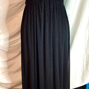 Puede incluir: Vestido de noche negro largo con tejido brillante y con purpurina. El vestido presenta un escote en V, tirantes finos y un corpi&ntilde;o fruncido. La falda llega hasta el suelo.