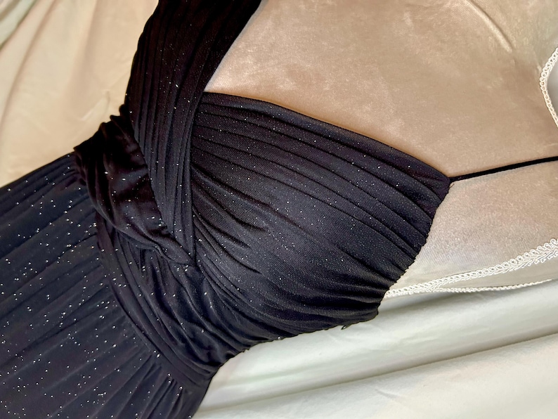 Puede incluir: Un vestido de noche negro y brillante con un corpi&ntilde;o drapeado y una silueta ajustada. El vestido presenta un cuello halter y una falda fluida, perfecto para eventos formales. La tela tiene un brillo sutil, agregando un toque de glamour.
