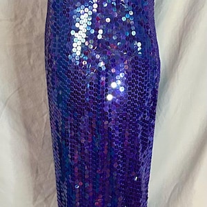 May include: A floor-length, sleeveless gown covered in iridescent blue sequins. The dress has a halter neckline and a form-fitting silhouette. The sequins create a shimmering effect, reflecting light. The dress is displayed on a mannequin.