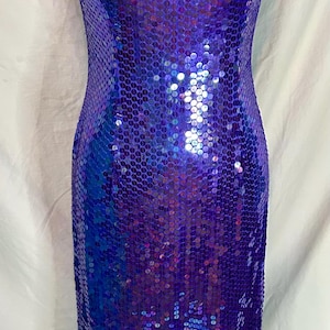May include: A floor-length, form-fitting dress covered in iridescent blue and purple sequins. The dress features a halter neckline with a keyhole cutout. The sequins create a shimmering effect, reflecting light.