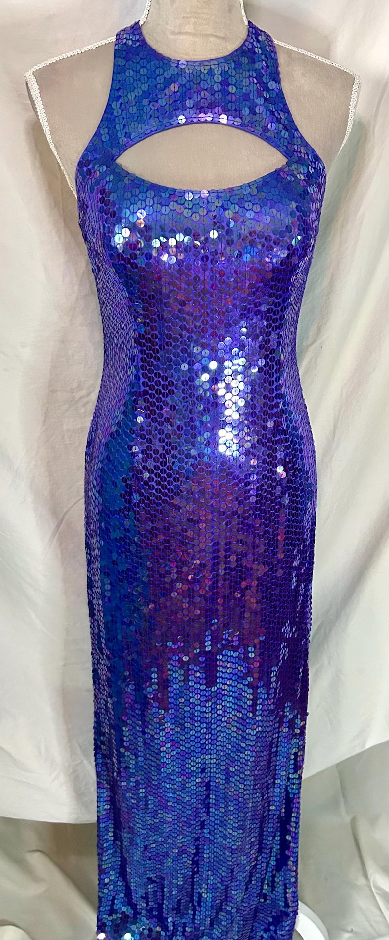 May include: A floor-length, form-fitting dress covered in iridescent blue and purple sequins. The dress features a halter neckline with a keyhole cutout. The sequins create a shimmering effect, reflecting light.