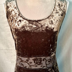 May include: A sleeveless dress made of crushed velvet in a deep brown color. The garment features a round neckline and a horizontal band across the waist area that displays a darker brown floral vine pattern against a semi-sheer fabric base.