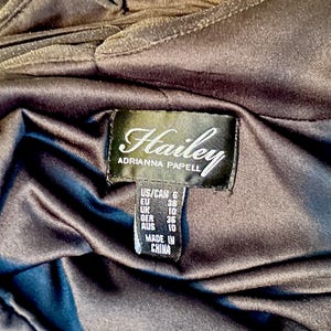 Puede incluir: Primer plano de una prenda marr&oacute;n oscuro con una etiqueta que dice "Hailey ADRIANNA PAPELL". La etiqueta tambi&eacute;n incluye informaci&oacute;n de tallas para US/CAN, EU, UK, GER y AUS. La prenda est&aacute; hecha en China.