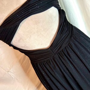 Puede incluir: Un vestido negro sin tirantes con la espalda descubierta. El vestido presenta un corpi&ntilde;o fruncido y una falda fluida. La tela tiene un brillo sutil, a&ntilde;adiendo un toque de glamour. El vestido est&aacute; dise&ntilde;ado para ocasiones formales.