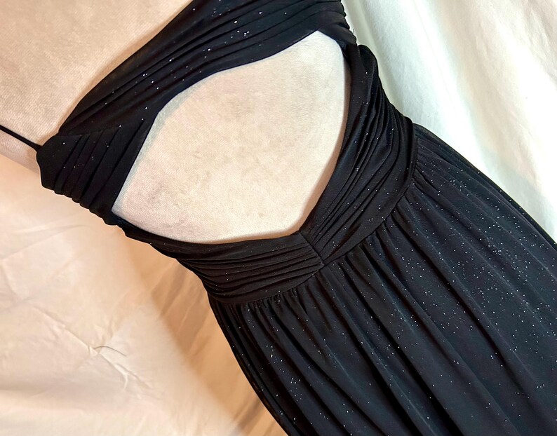Puede incluir: Un vestido negro sin tirantes con la espalda descubierta. El vestido presenta un corpi&ntilde;o fruncido y una falda fluida. La tela tiene un brillo sutil, a&ntilde;adiendo un toque de glamour. El vestido est&aacute; dise&ntilde;ado para ocasiones formales.