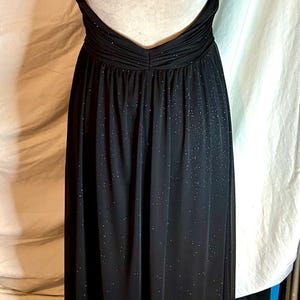 Puede incluir: Un vestido de noche negro con una falda fluida y tirantes finos. El vestido presenta una espalda descubierta y est&aacute; adornado con peque&ntilde;os detalles brillantes en toda la tela. El vestido se exhibe en un maniqu&iacute;.