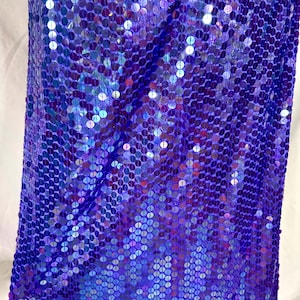 May include: A close-up of a fabric covered in iridescent blue and purple sequins. The sequins are round and densely packed, creating a shimmering effect. The fabric is likely used for apparel or decorative purposes.