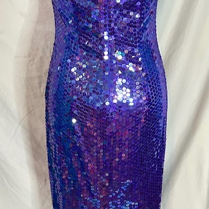 May include: A shimmering, floor-length gown in shades of purple and blue. The dress is covered in sequins, creating a dazzling effect. It features a halter neckline and a slit in the back, adding a touch of elegance.
