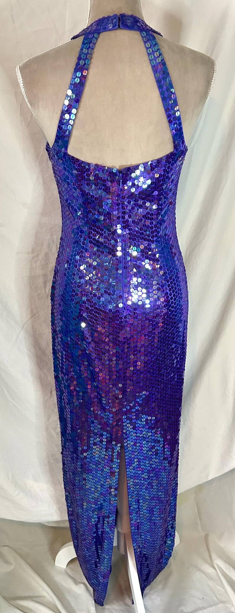 May include: A shimmering, floor-length gown in shades of purple and blue. The dress is covered in sequins, creating a dazzling effect. It features a halter neckline and a slit in the back, adding a touch of elegance.