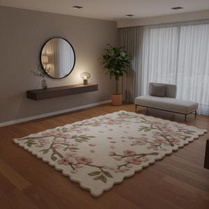 May include: A cream-colored area rug with a floral design featuring pink blossoms and green leaves. The rug is rectangular with a scalloped edge, placed on a hardwood floor in a well-lit room. The room also features a mirror, a bench, and a plant.