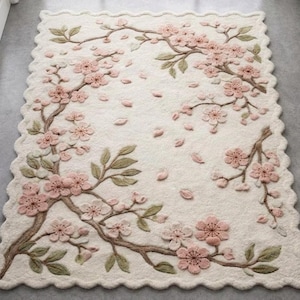 May include: Cream-colored rectangular rug with a scalloped edge, featuring a 3D floral design. Pink cherry blossoms and falling petals are arranged on brown branches with green leaves, creating a nature-inspired home decor piece.